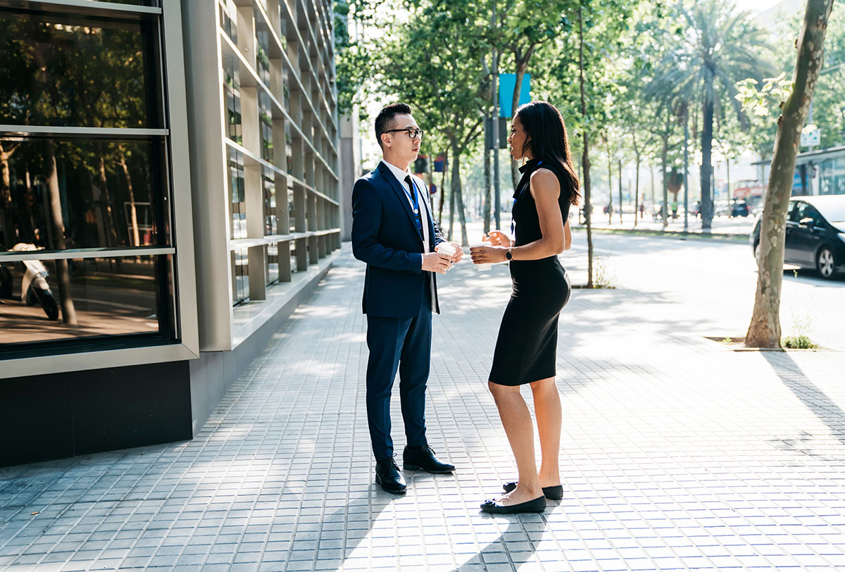 Male and female office workers conversing on a modern city street.